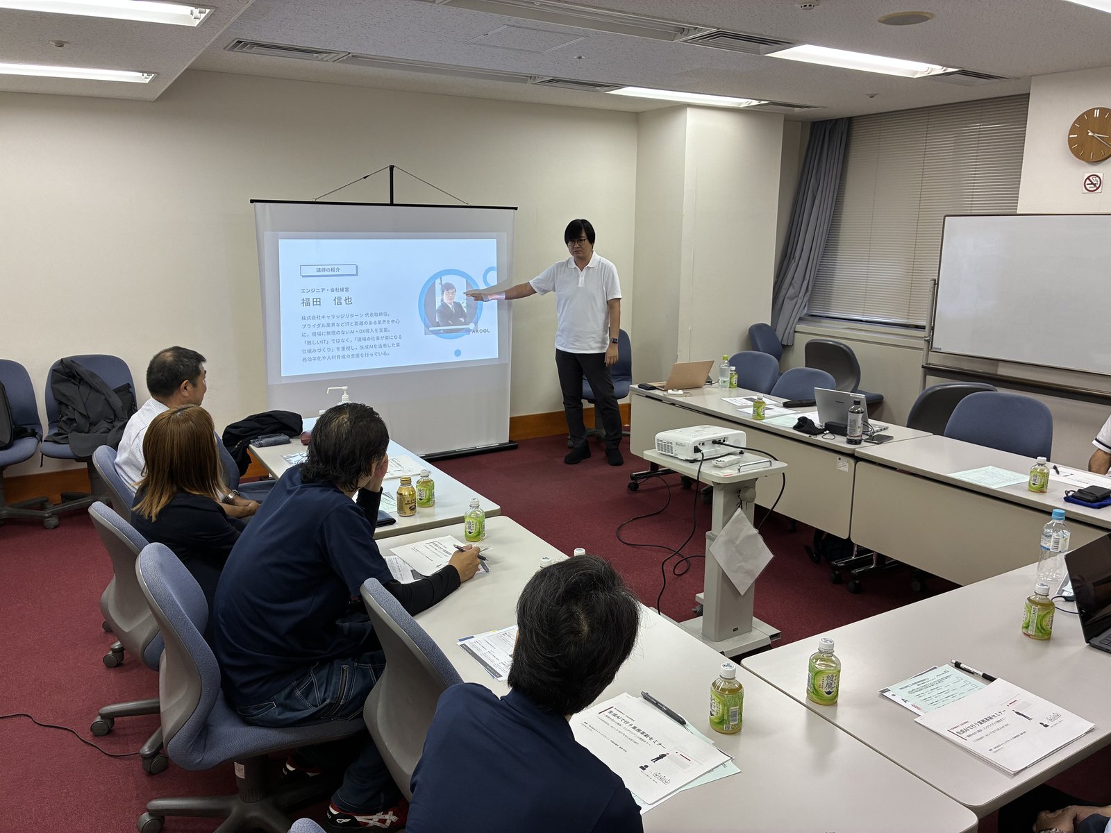 スクリーンに投影した講師紹介スライドを示しながら説明する講師の福田信也